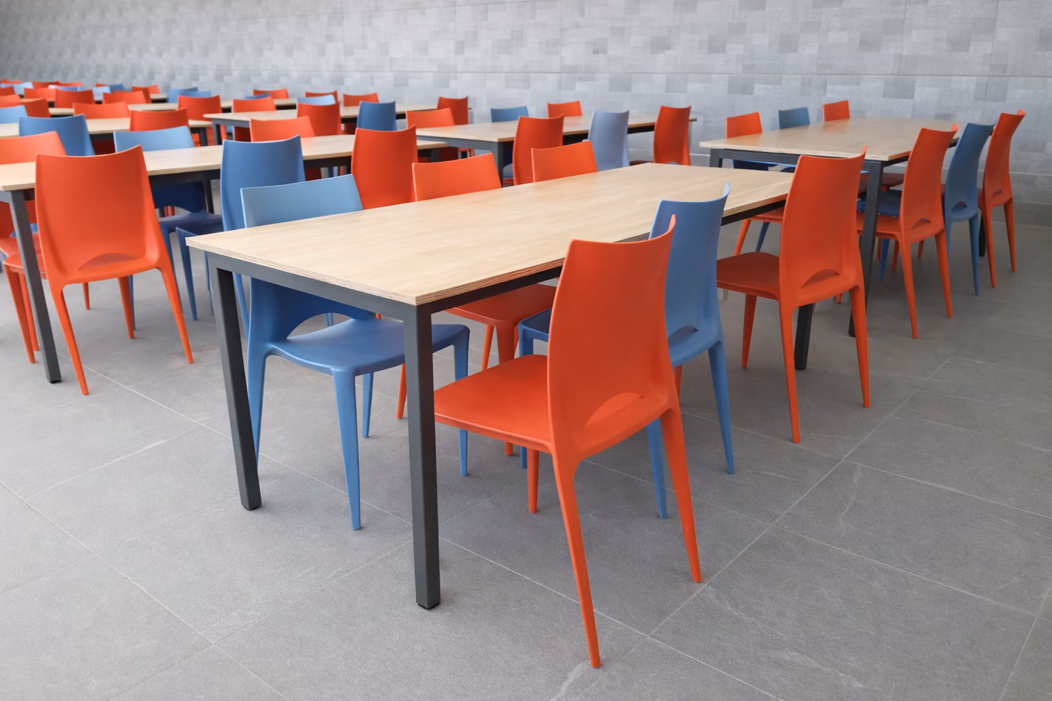 Comedor de casino con mesas de cubierta de madera y sillas rojas y azules