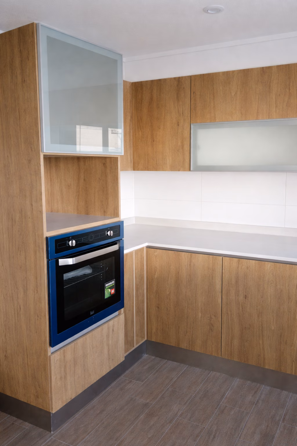 Columna de horno empotrado y muebles altos con puertas de vidrio en una cocina a medida