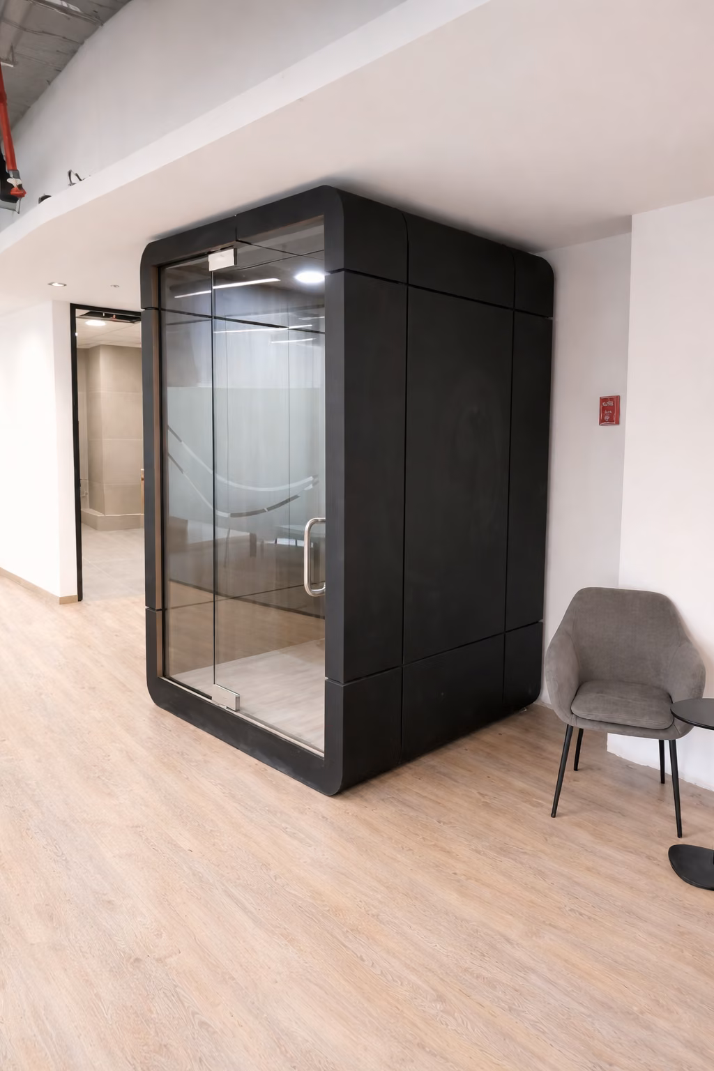 Cabina acústica negra con sillón gris en una zona de estar