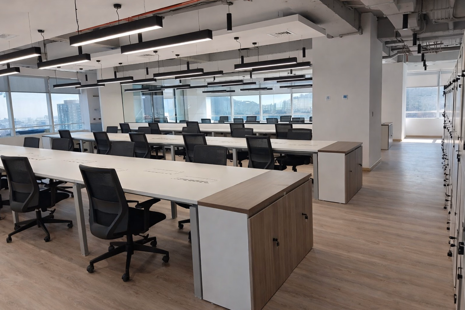 Open space con estaciones de trabajo blancas frente a ventanales, Oficina Millenium