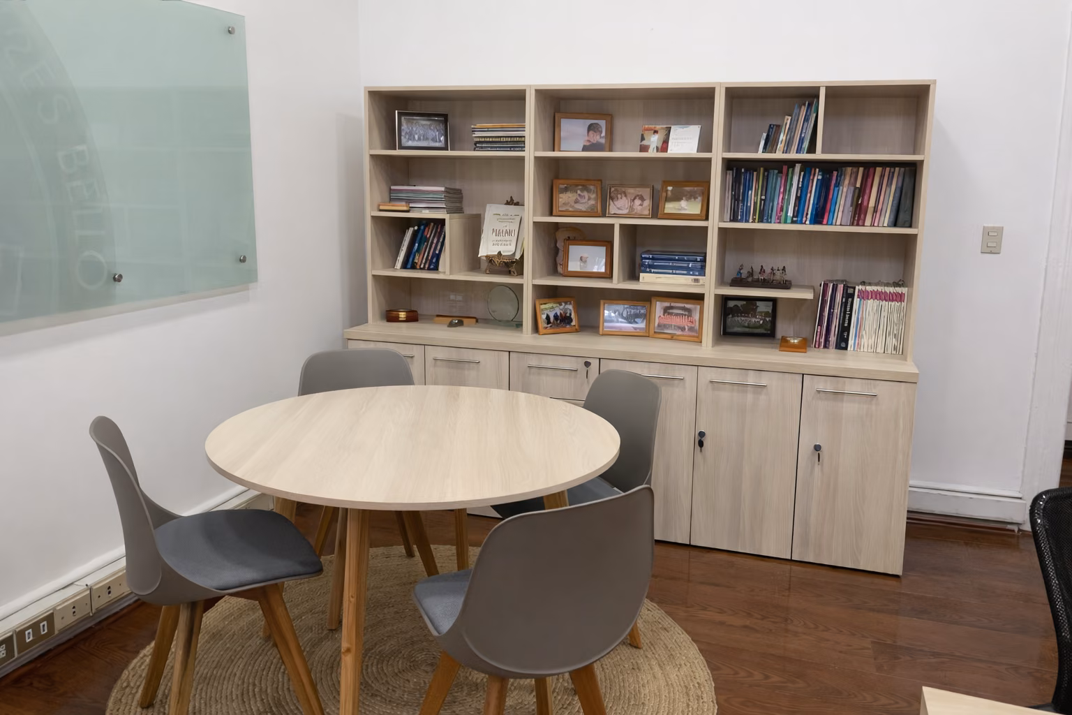 Mesa de reunión circular y biblioteca de madera clara en una oficina universitaria