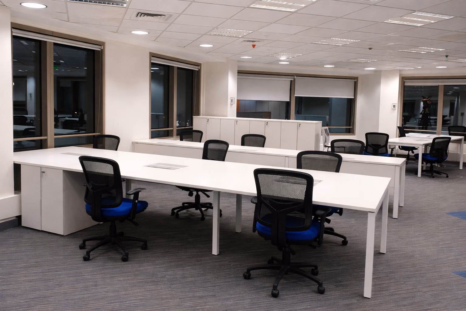 Estaciones bench blancas con sillas azules frente a ventanales, Oficina Santiago Centro