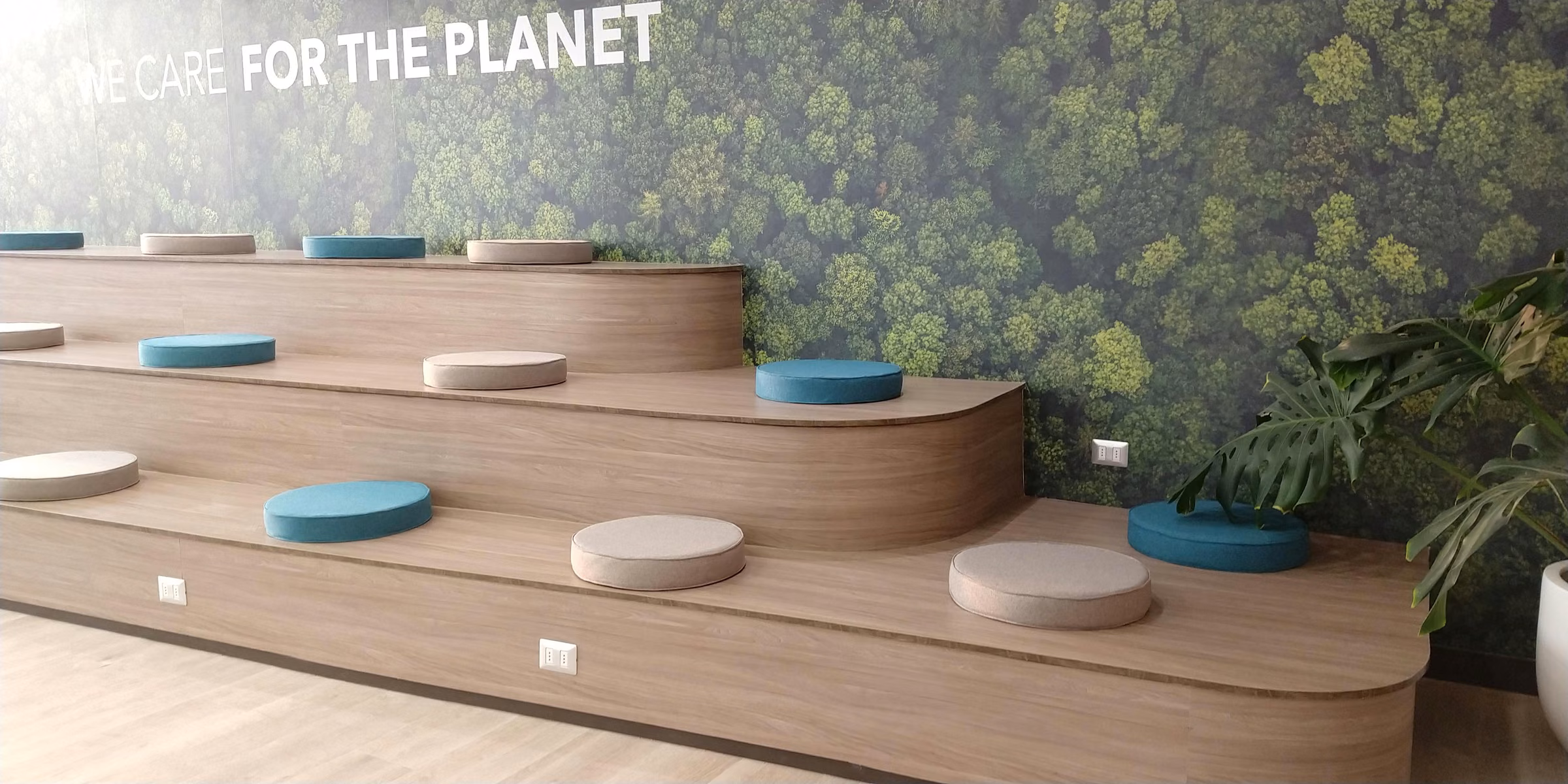 Gradas de madera con cojines tapizados en azul petróleo y beige frente a un muro vegetal, auditorio de Oficina Titanium
